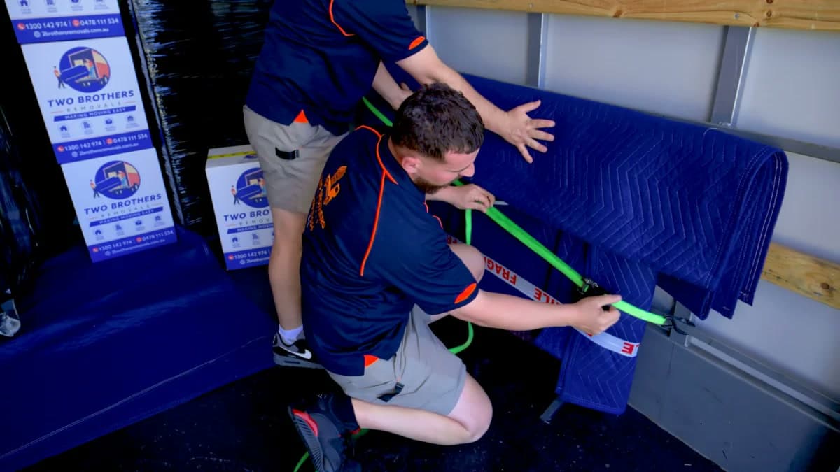 Removalists securing padded furniture with heavy-duty ratchet straps inside the truck