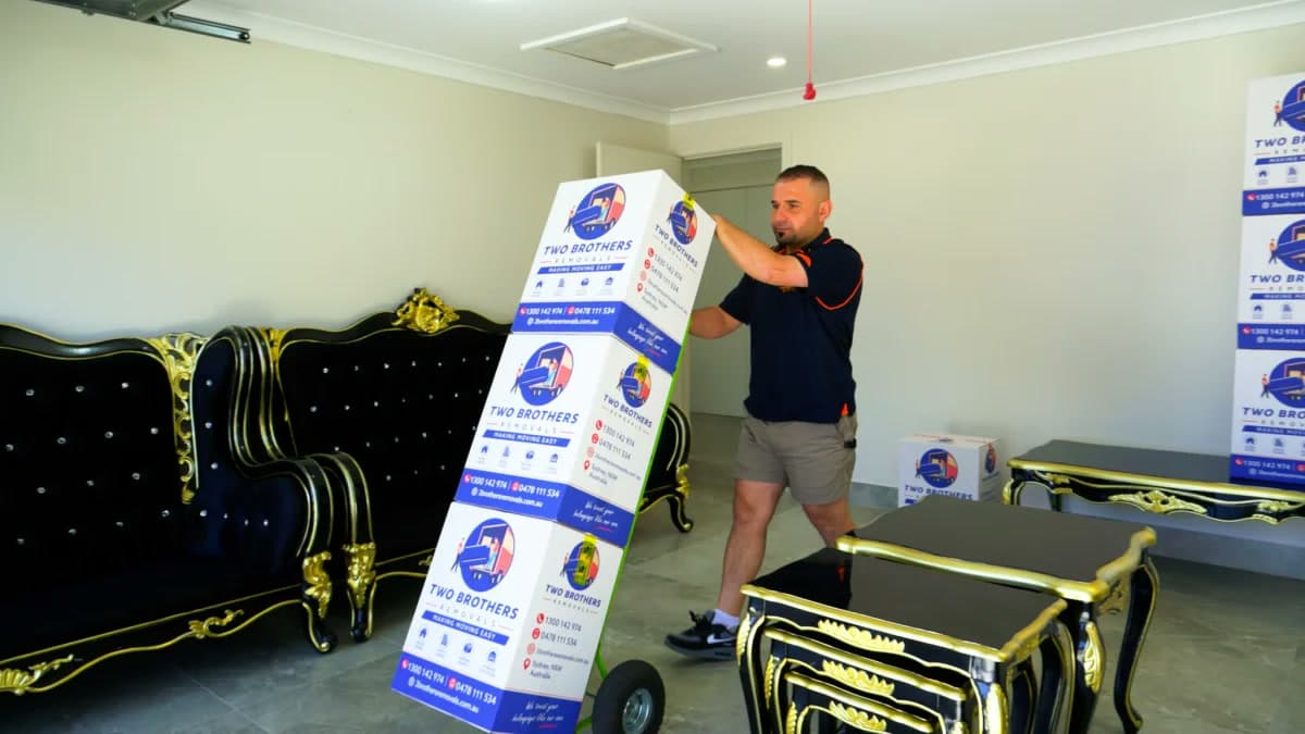 Removalist wheeling stacked Two Brothers boxes on a hand trolley through the living room