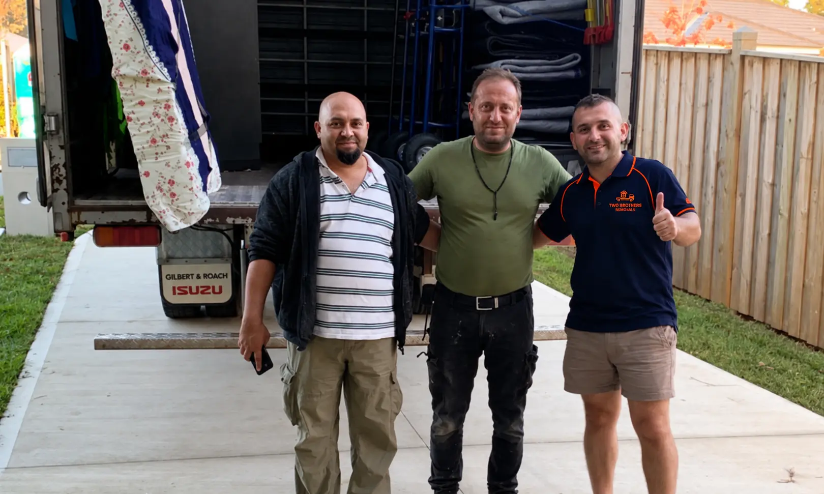Removalist giving a thumbs up with happy customers at the back of the moving truck