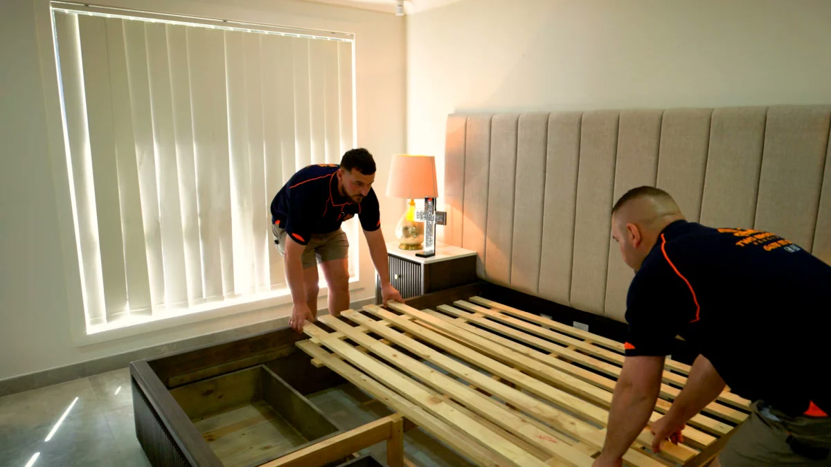Removalists assembling timber bed slats onto the bed frame in the bedroom