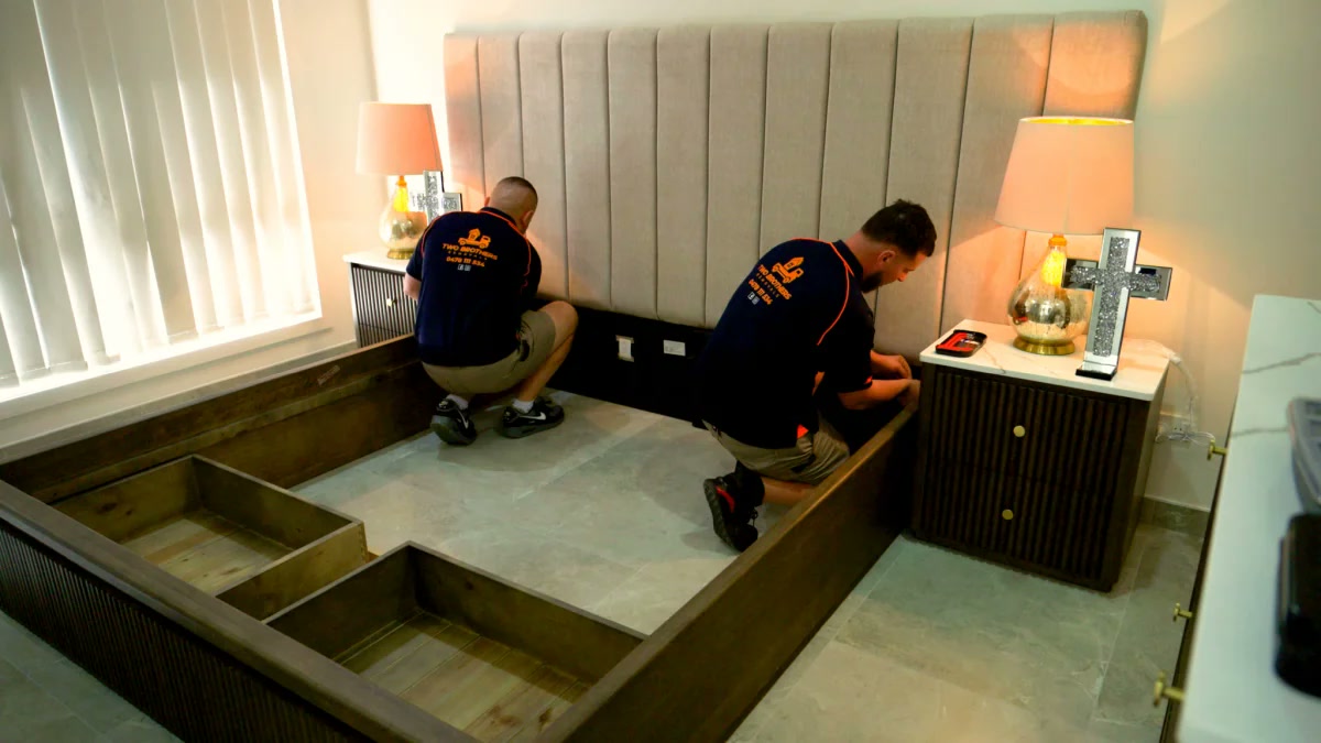 Removalists assembling a custom timber bed frame with built-in storage drawers