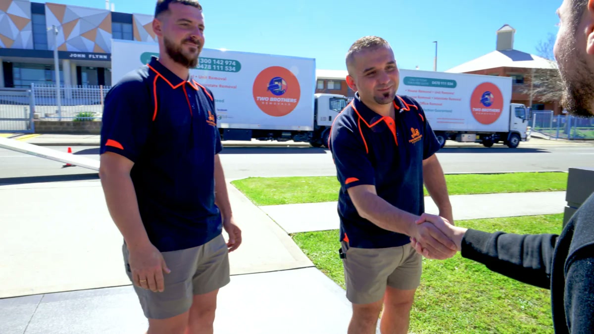 Two Brothers removalists shaking hands with a satisfied customer with trucks parked outside