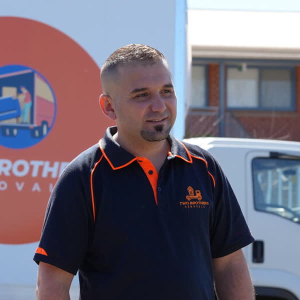 Nawar, co-founder of Two Brothers Removals, in an orange-and-navy polo in front of the company truck